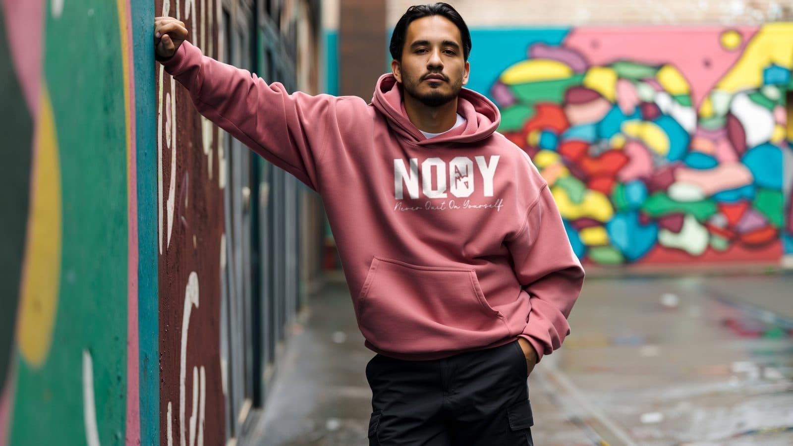 A man wearing an NQOY hoodie against a painted mural wall